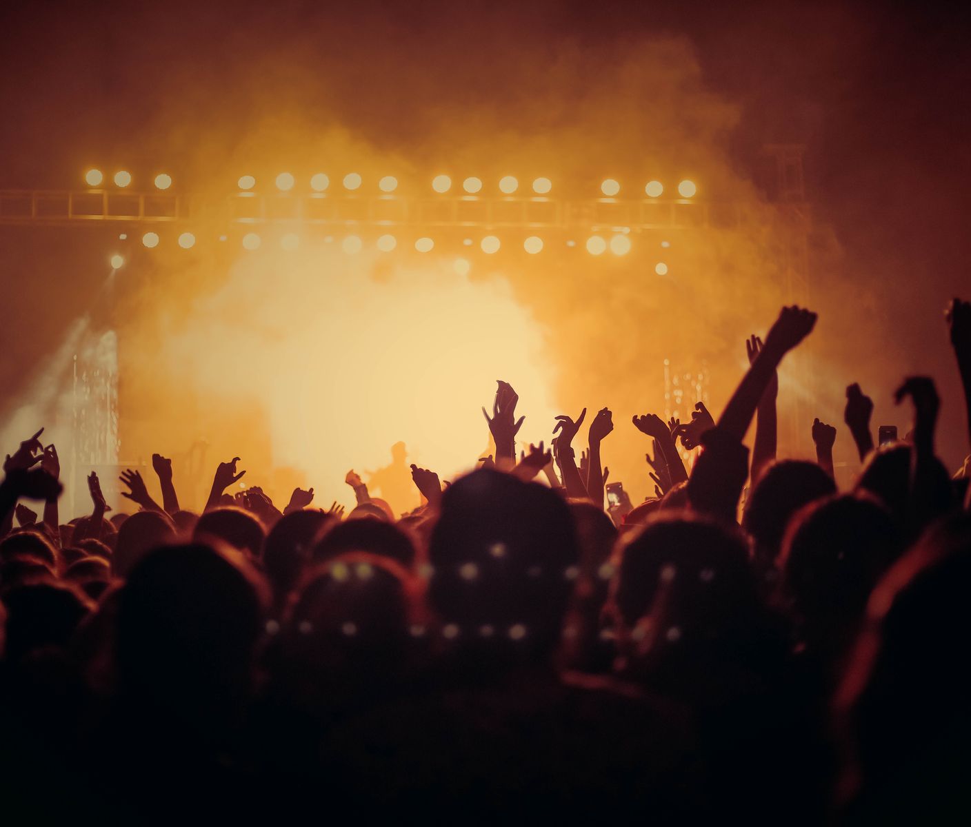 A concert crowd with hands raised in front of warm stage lights